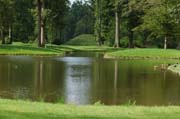 Hinter dem Wasser wirkt der Erdkegel im Queen-Auguste-Victoria-Park beruhigend und sanft